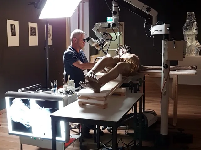 Restaurátor nagyítóoptika alatt vizsgálja és dokumentálja egy műemléki szobor állapotát